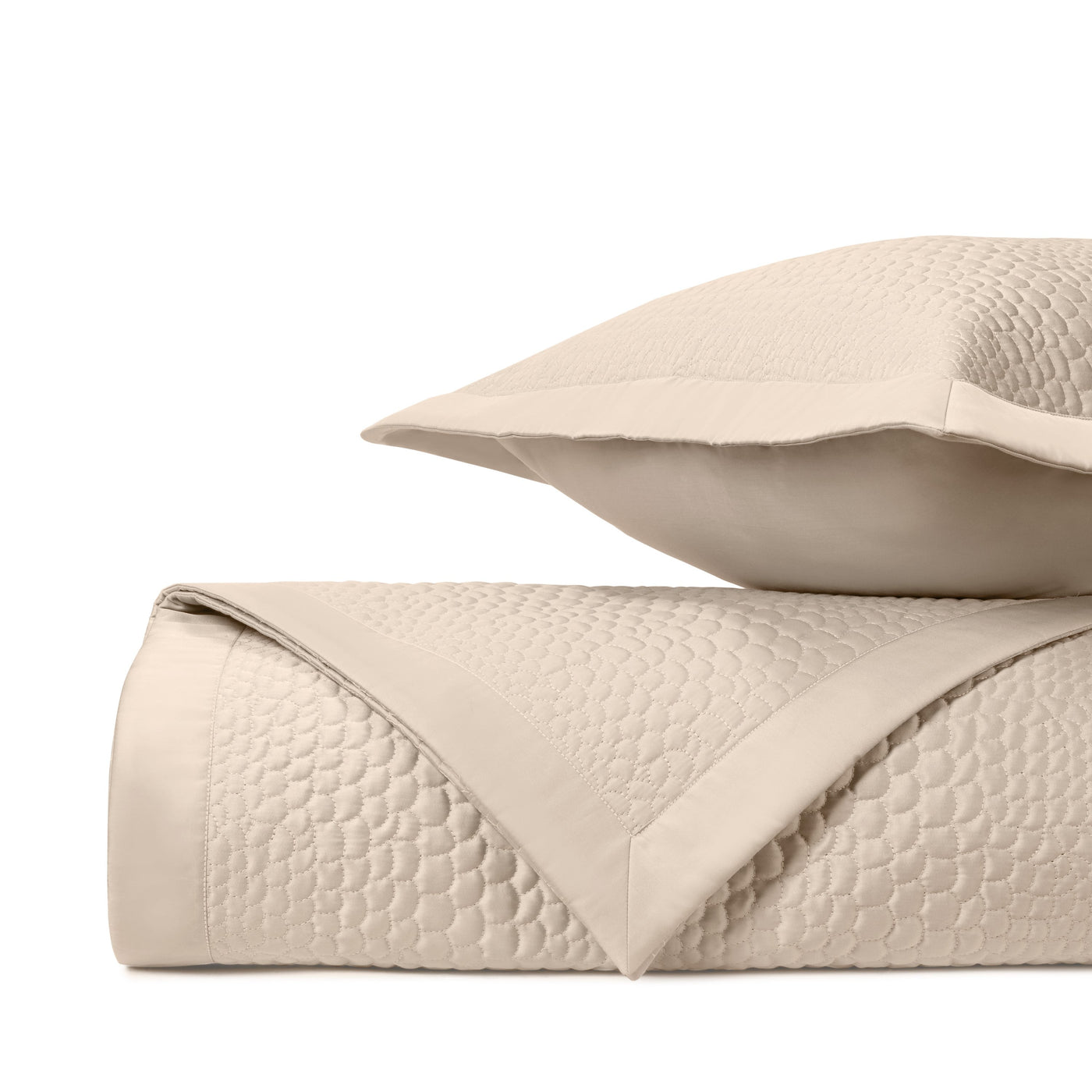 Ivory quilted coverlet folded with matching sham, showing honeycomb stitch pattern detail.