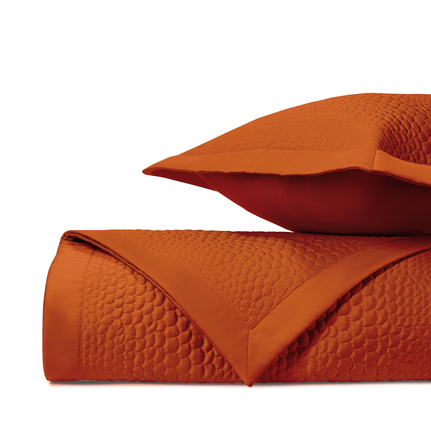 Burnt orange quilted texture detail showing honeycomb stitch pattern on folded coverlet.