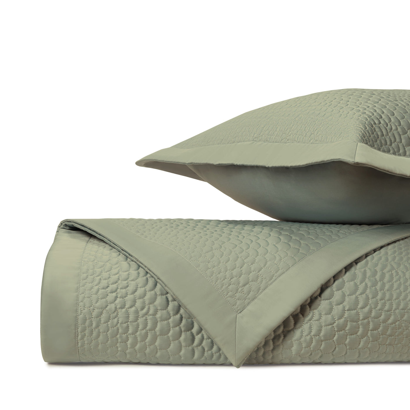 Close-up of sage green quilted texture with honeycomb pattern on folded coverlet and sham.