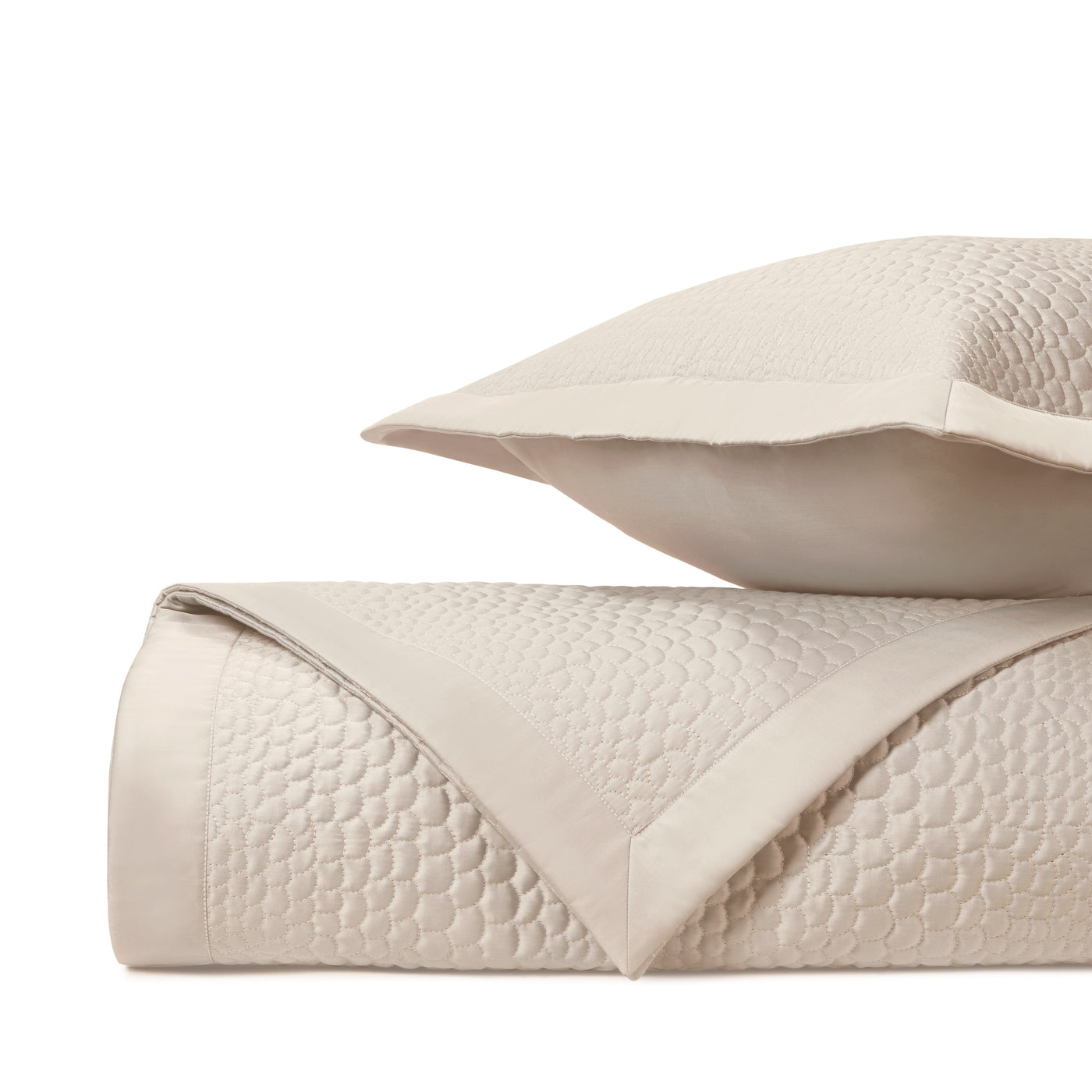 Ivory quilted coverlet and sham stack showing geometric honeycomb texture detail.