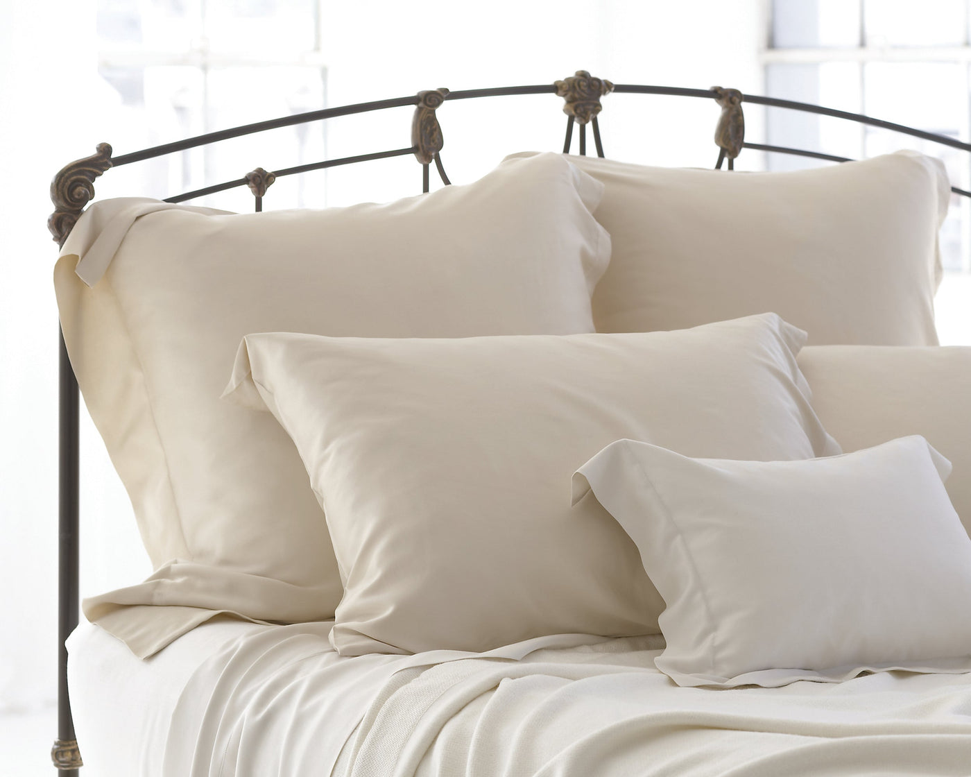 Legna Classic ivory decorative pillow styled on bed with matching euro shams and iron headboard.
