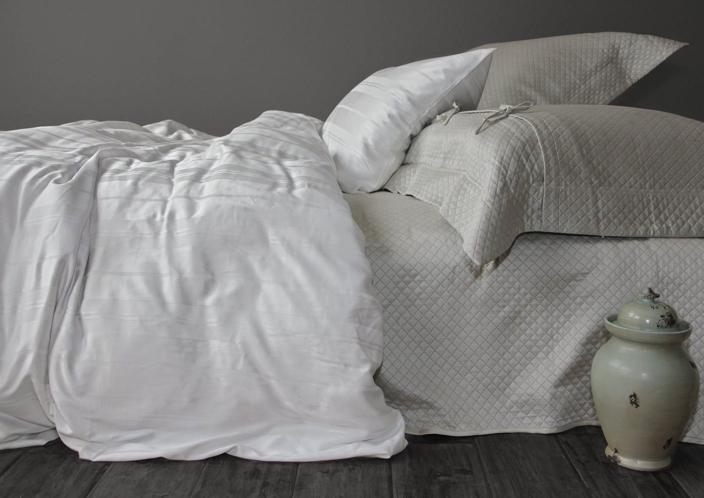 Ivory quilted bedskirt on styled bed with white duvet and ceramic urn accent.