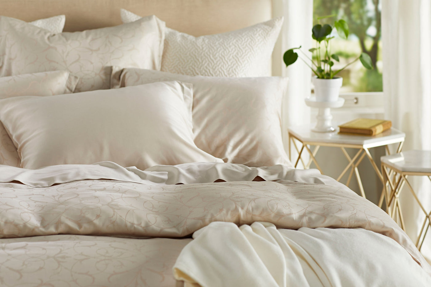 Close-up of Legna Seville decorative pillow in ivory with floral jacquard pattern on styled bed.