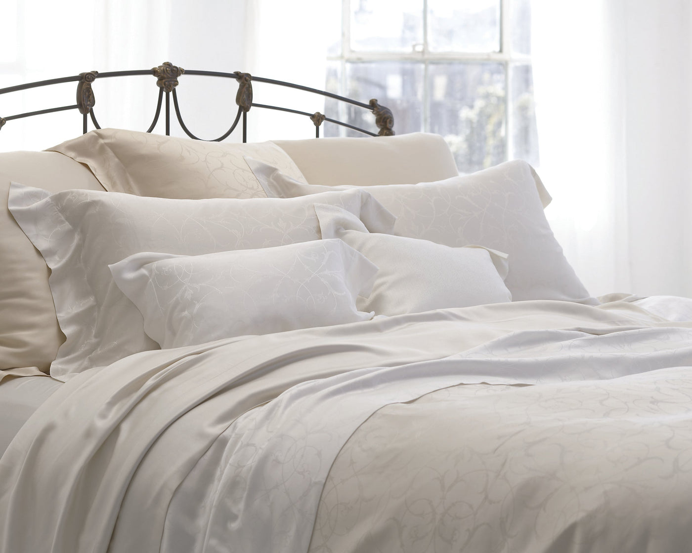 Legna Seville ivory decorative pillow styled on a bed with white and cream bedding.