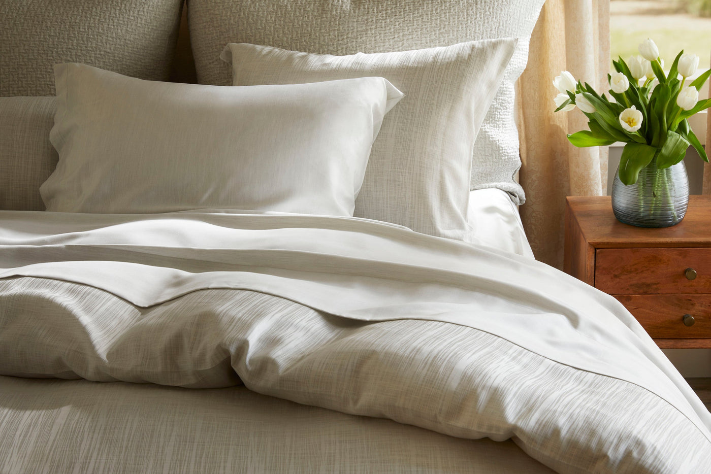 Legna Tigris bed skirt styled on bed with ivory textured duvet and white tulips.