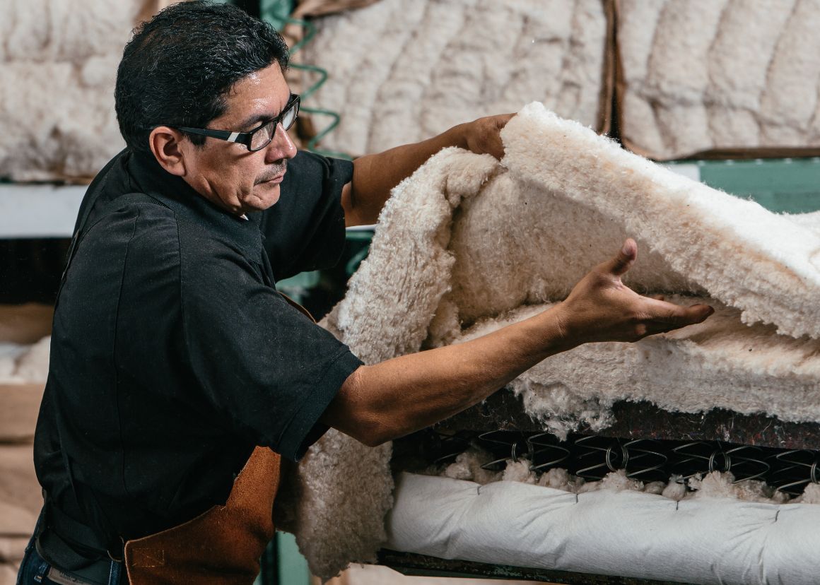 A craftsman laying a thick layer of natural cotton over mattress coils