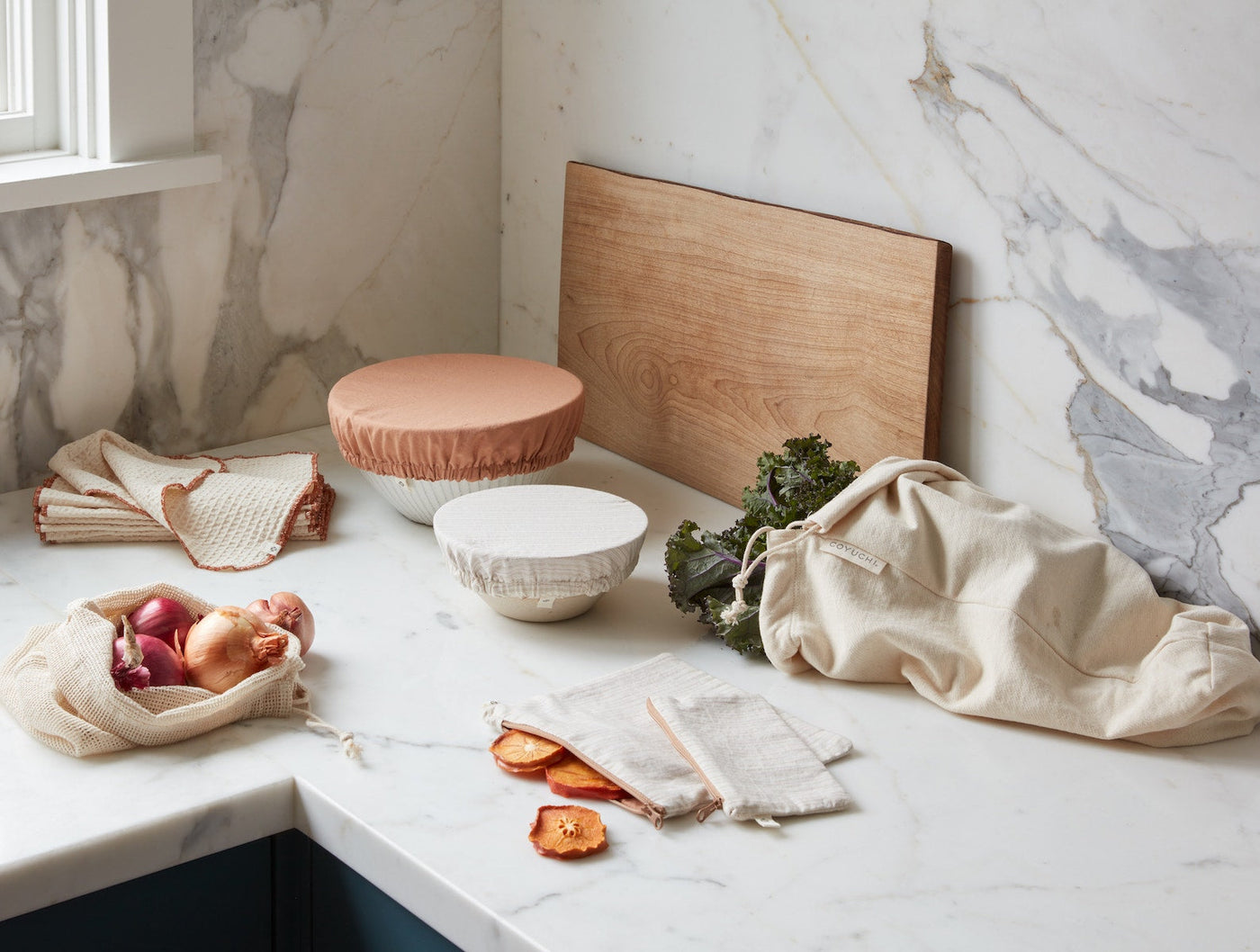 Natural linen produce bags styled on marble countertop with fresh vegetables and dried fruit.