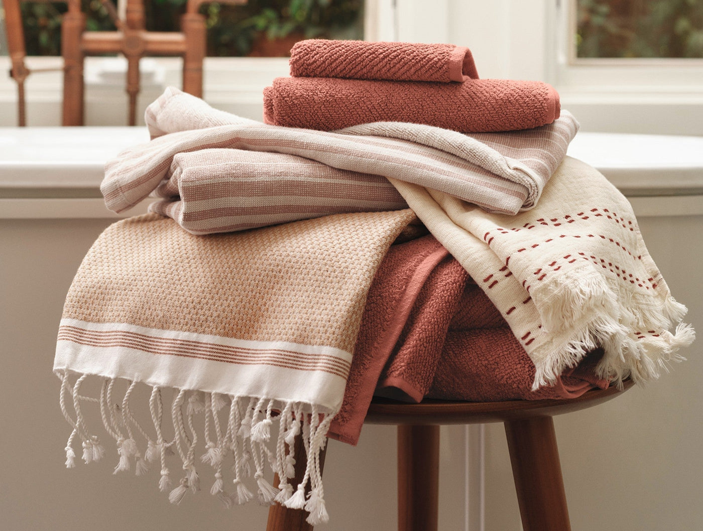 Terracotta and natural cotton bath towels stacked on a stool, with fringed hammam style draping.