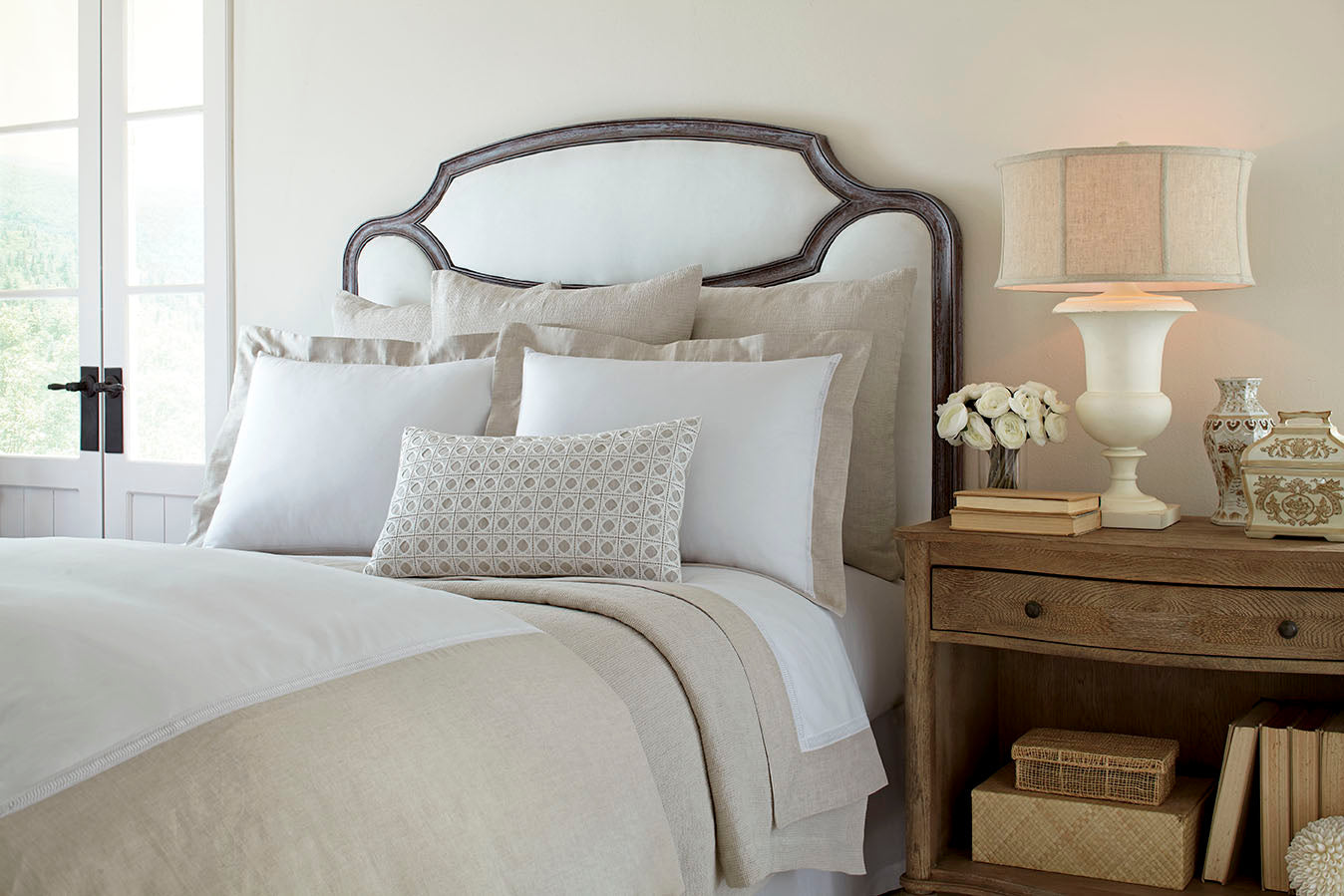 Home Treasures Linea bedding styled in ivory and sand on an upholstered bed.