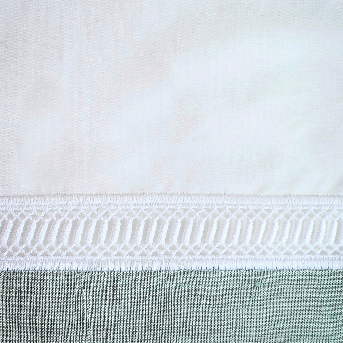 Close-up of white cotton fabric with delicate woven lace trim border detail.