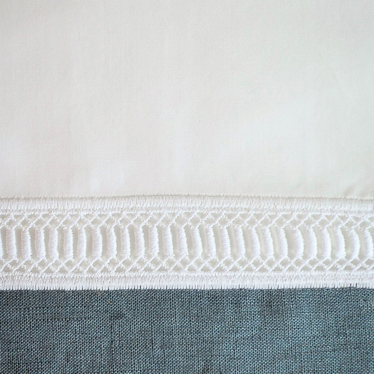 Close-up of ivory cotton hem with intricate woven ladder lace trim detail.