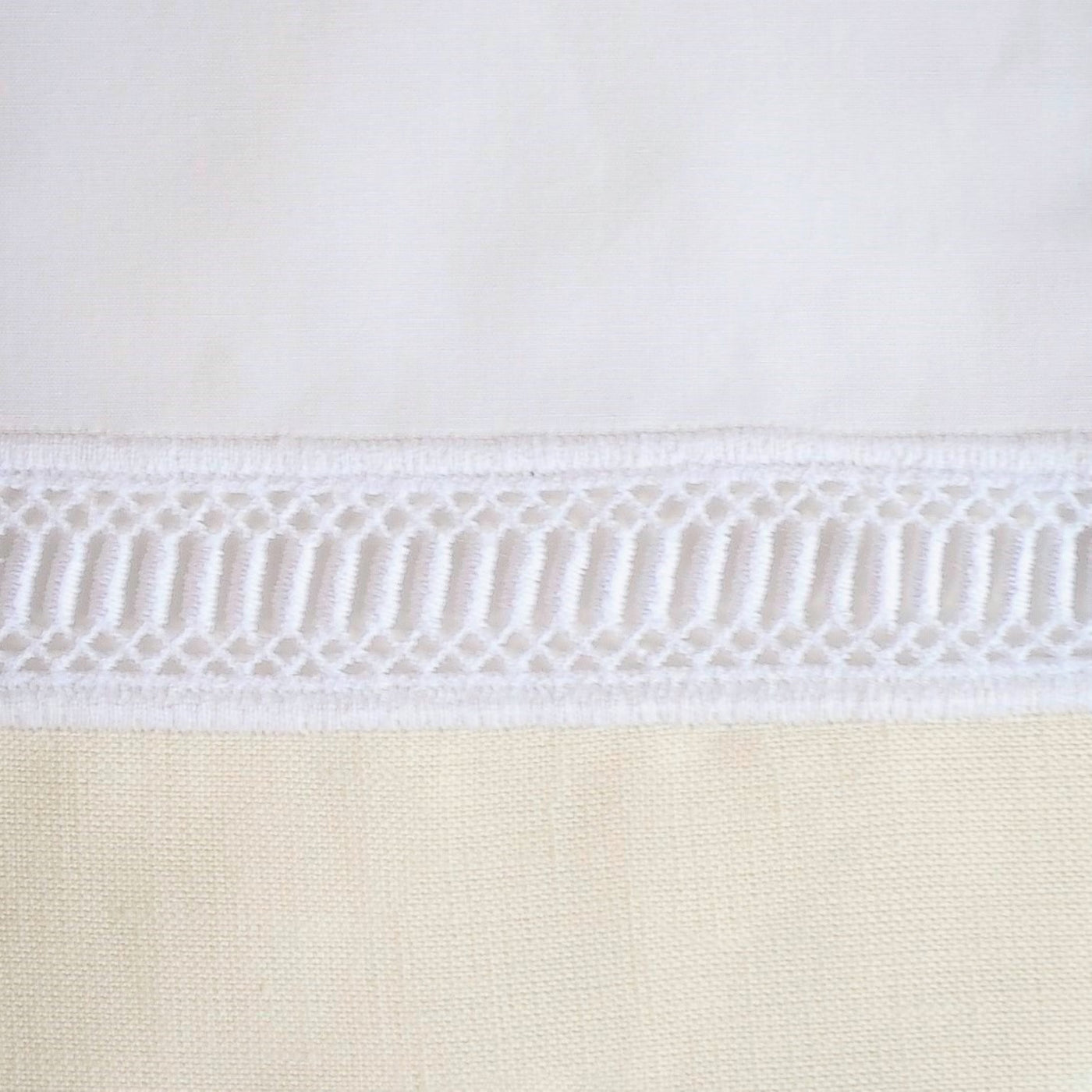 Close-up of white cotton trim with ladder-stitch lace border against ivory fabric.