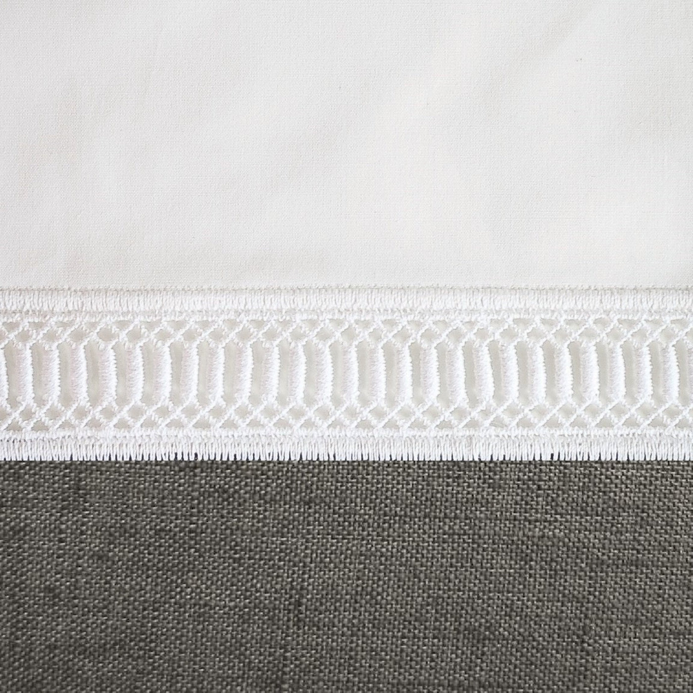 Close-up of white cotton hem with geometric ladder embroidery trim detail.