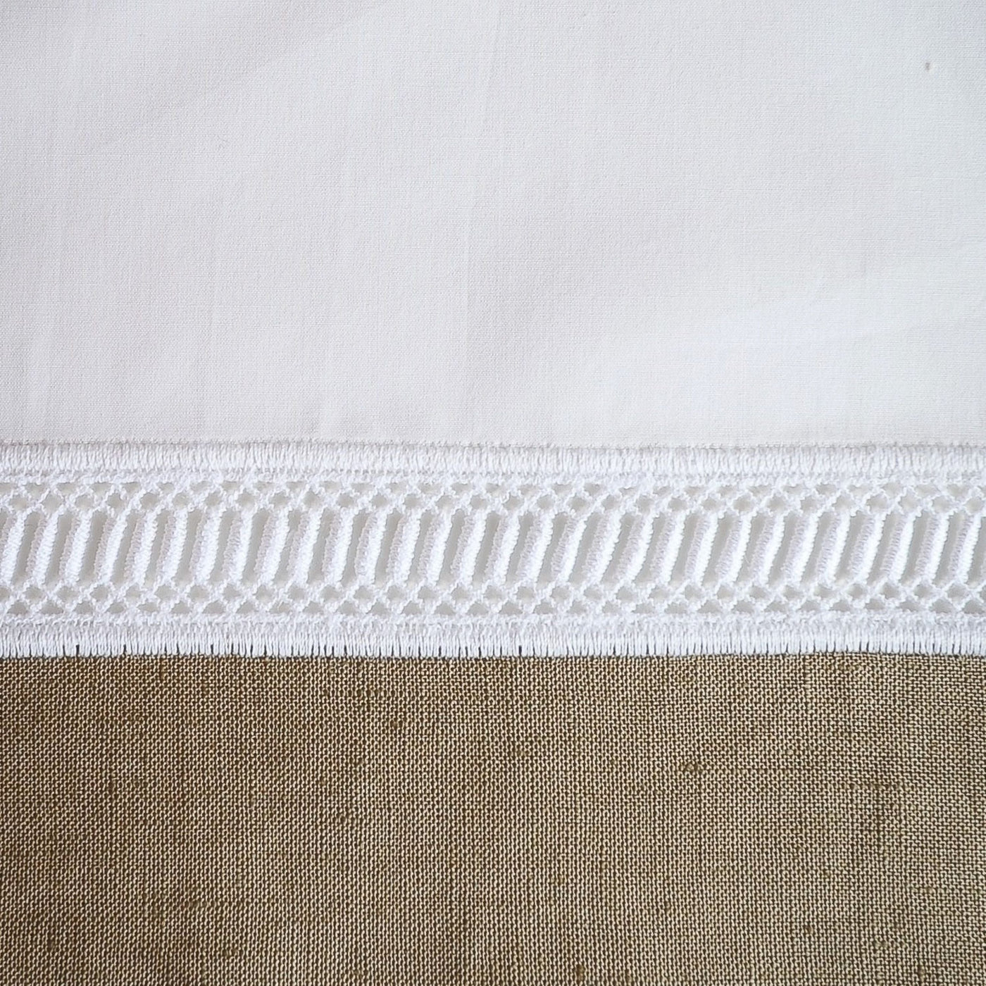Close-up of white cotton border with geometric macramé-style lace trim above natural linen panel.