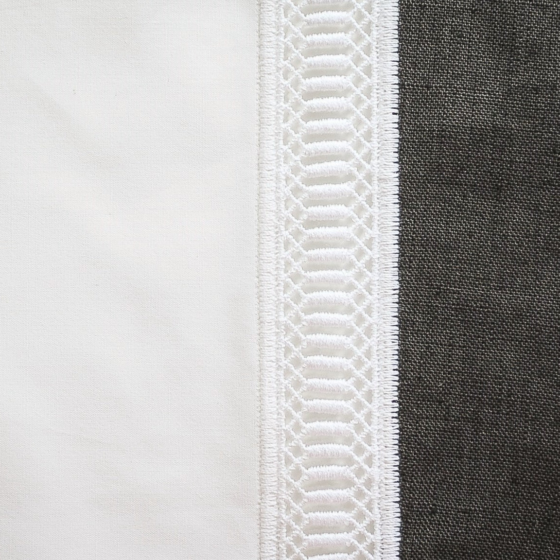 Close-up of ivory lace trim detailing against white and charcoal linen fabric.