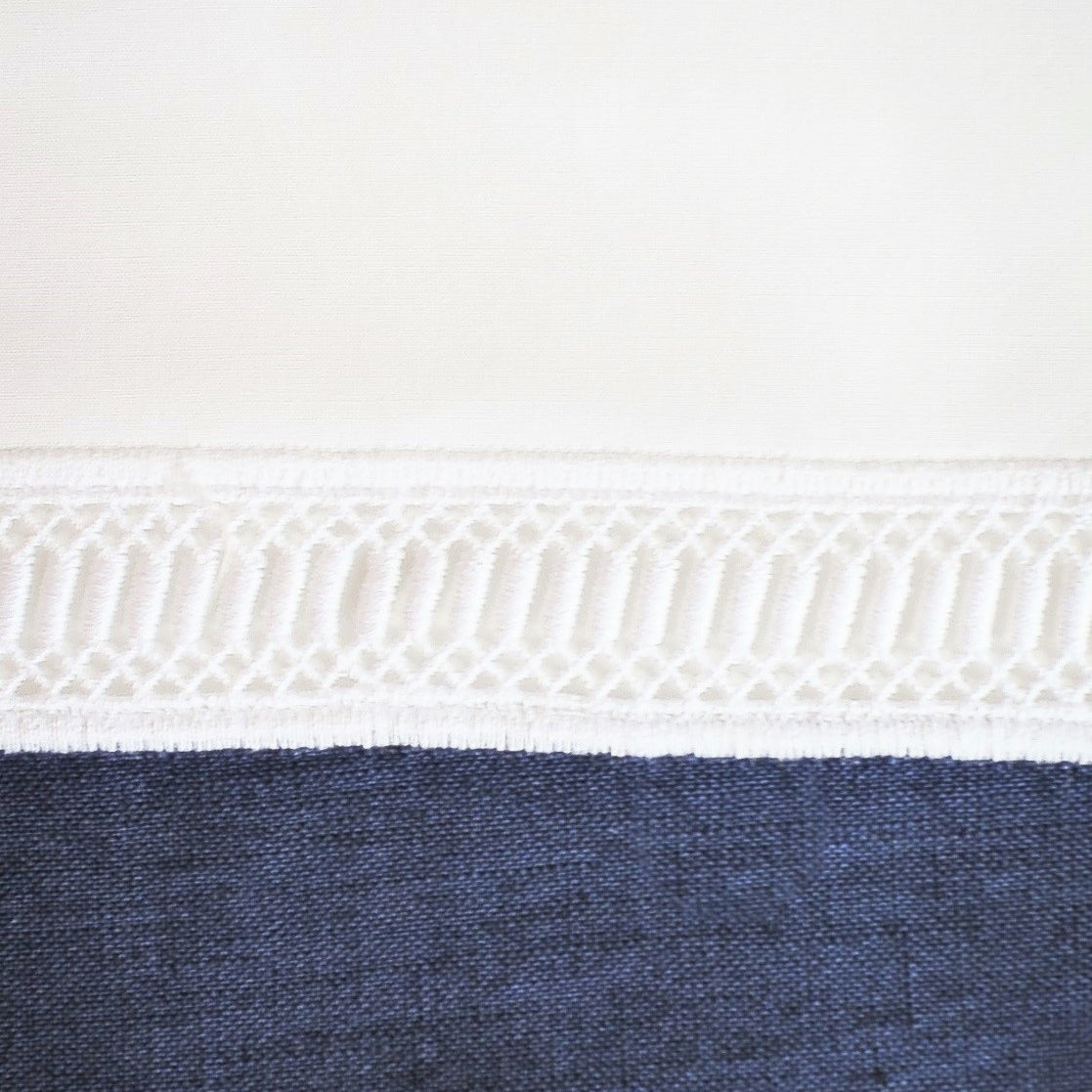 Close-up of ivory crochet lace trim bordering navy linen fabric on a pillow sham.