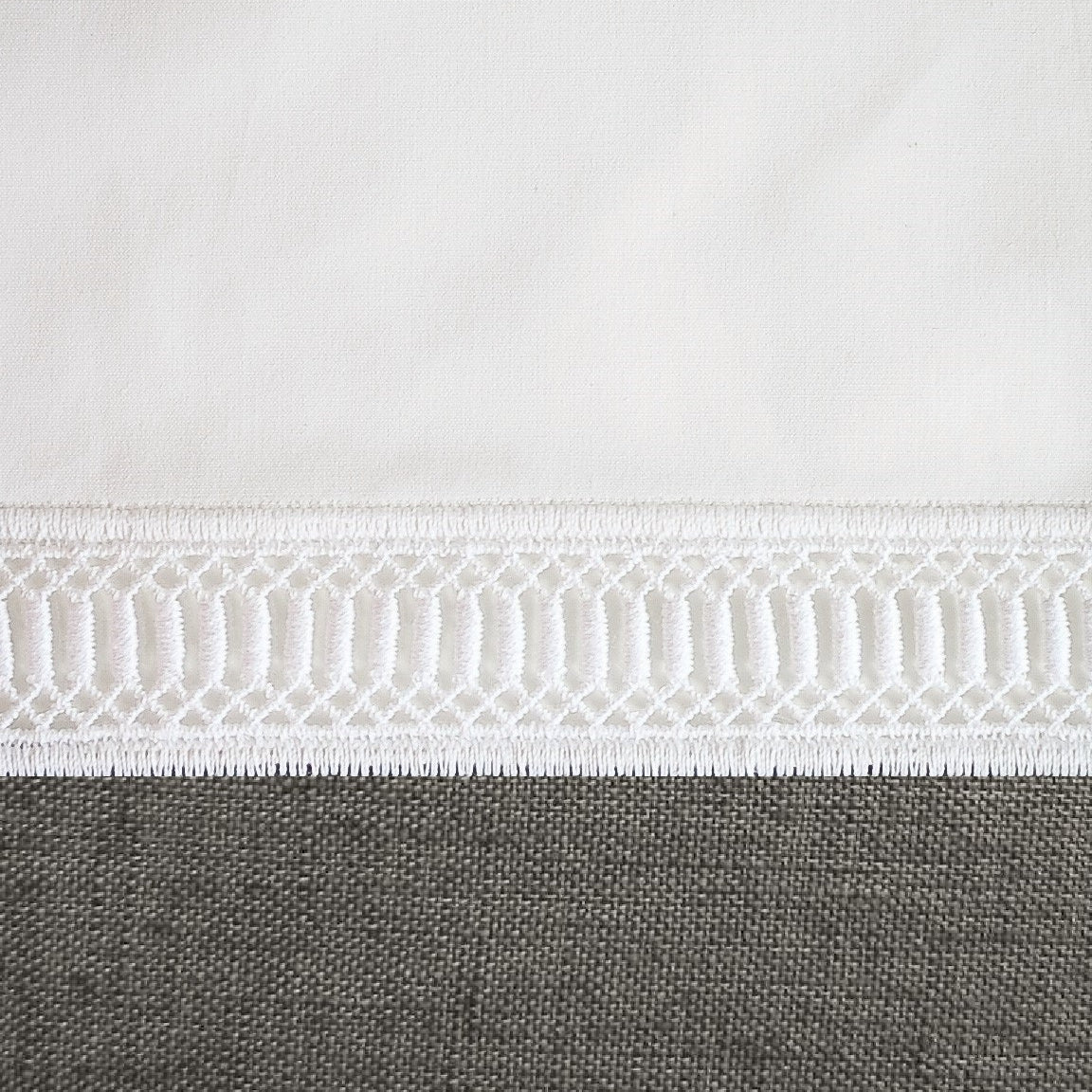 Close-up of geometric ladder lace trim along the hem of a white cotton pillow sham.