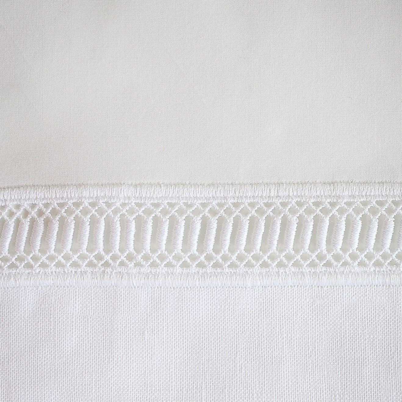 Close-up of ivory linen pillow sham with geometric lace trim border detail.