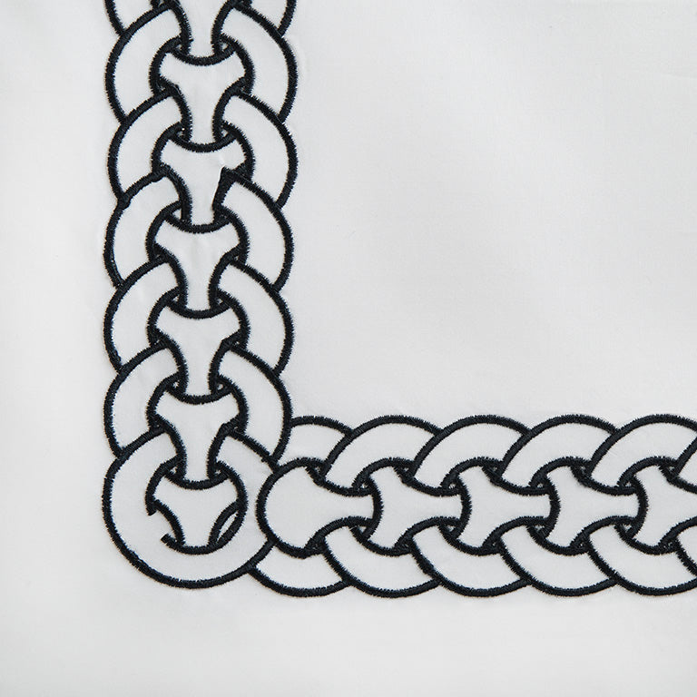 Close-up of navy chain-link embroidery border on white cotton pillowcase corner.