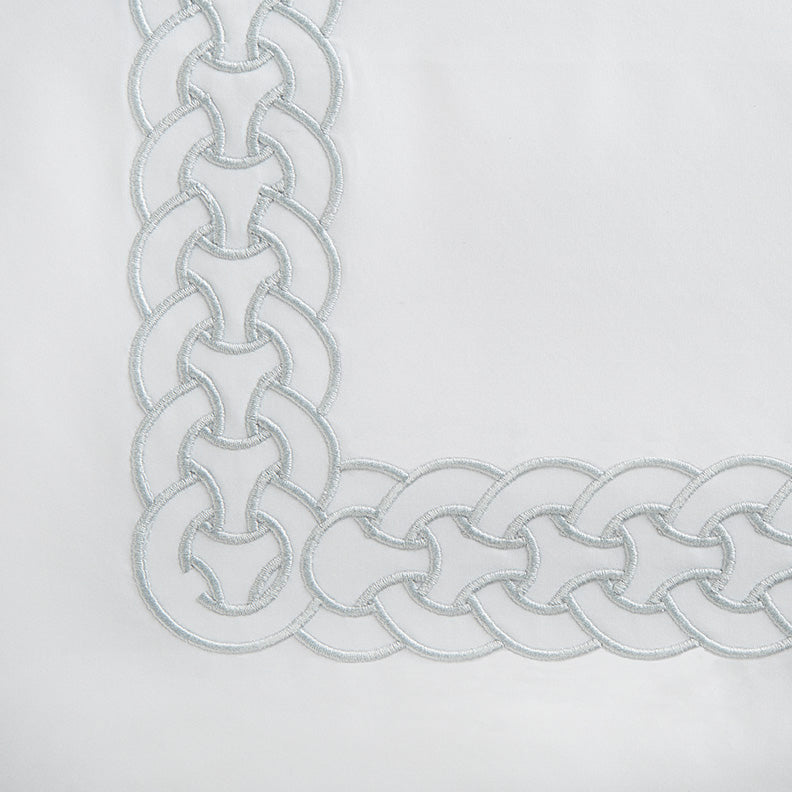 Close-up of interlocking chain embroidery border in silver-blue on white cotton.