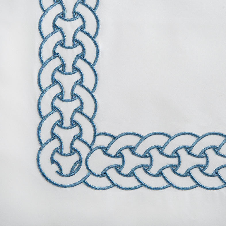 Corner detail of sky blue chain-link embroidery on white cotton fabric.