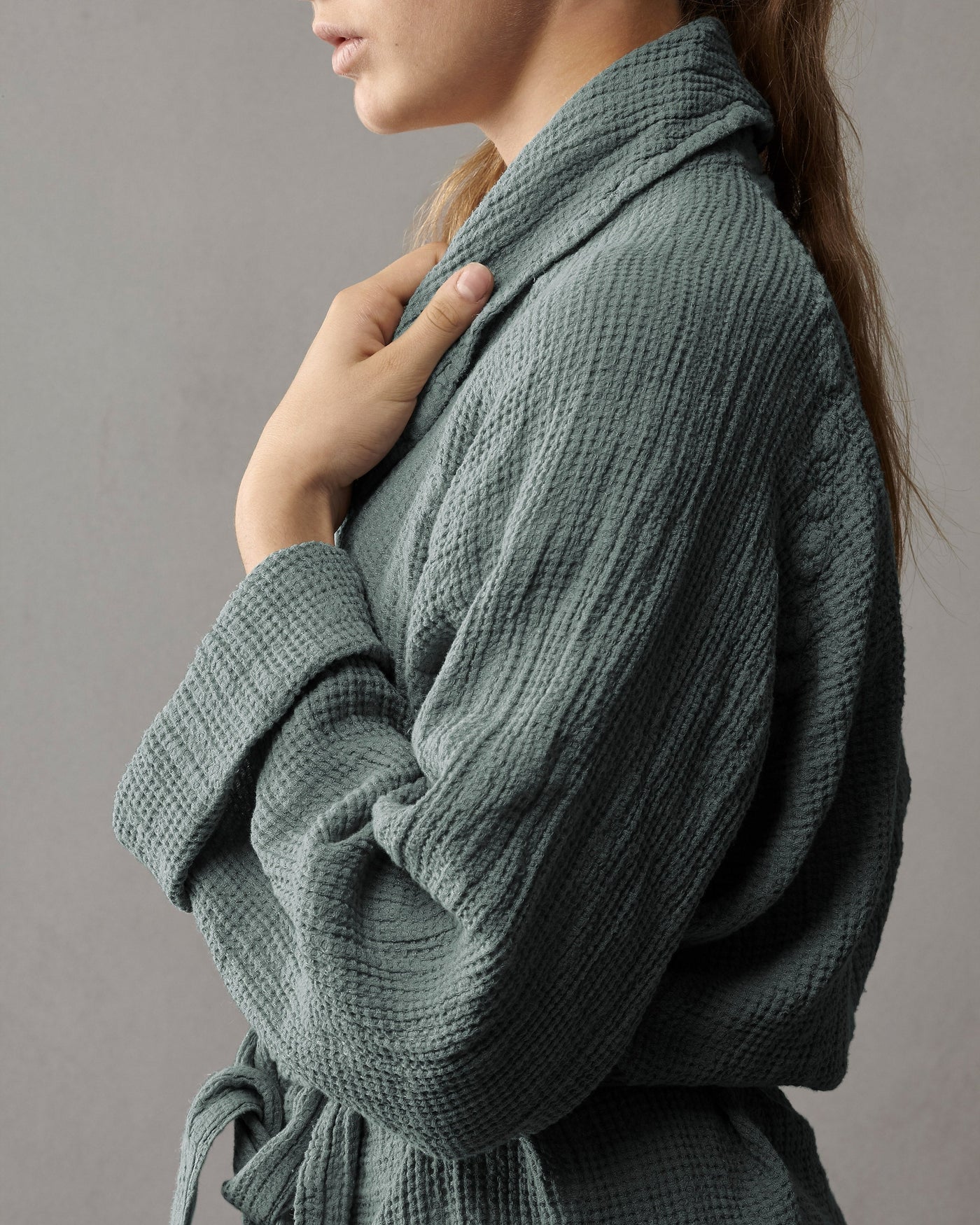 Close-up of sage green textured cotton robe with shawl collar, worn and belted at waist.