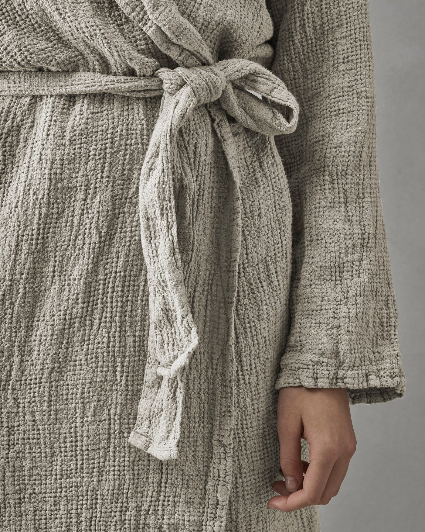 Close-up of knotted waist belt and cuffed sleeve in textured taupe cotton weave.