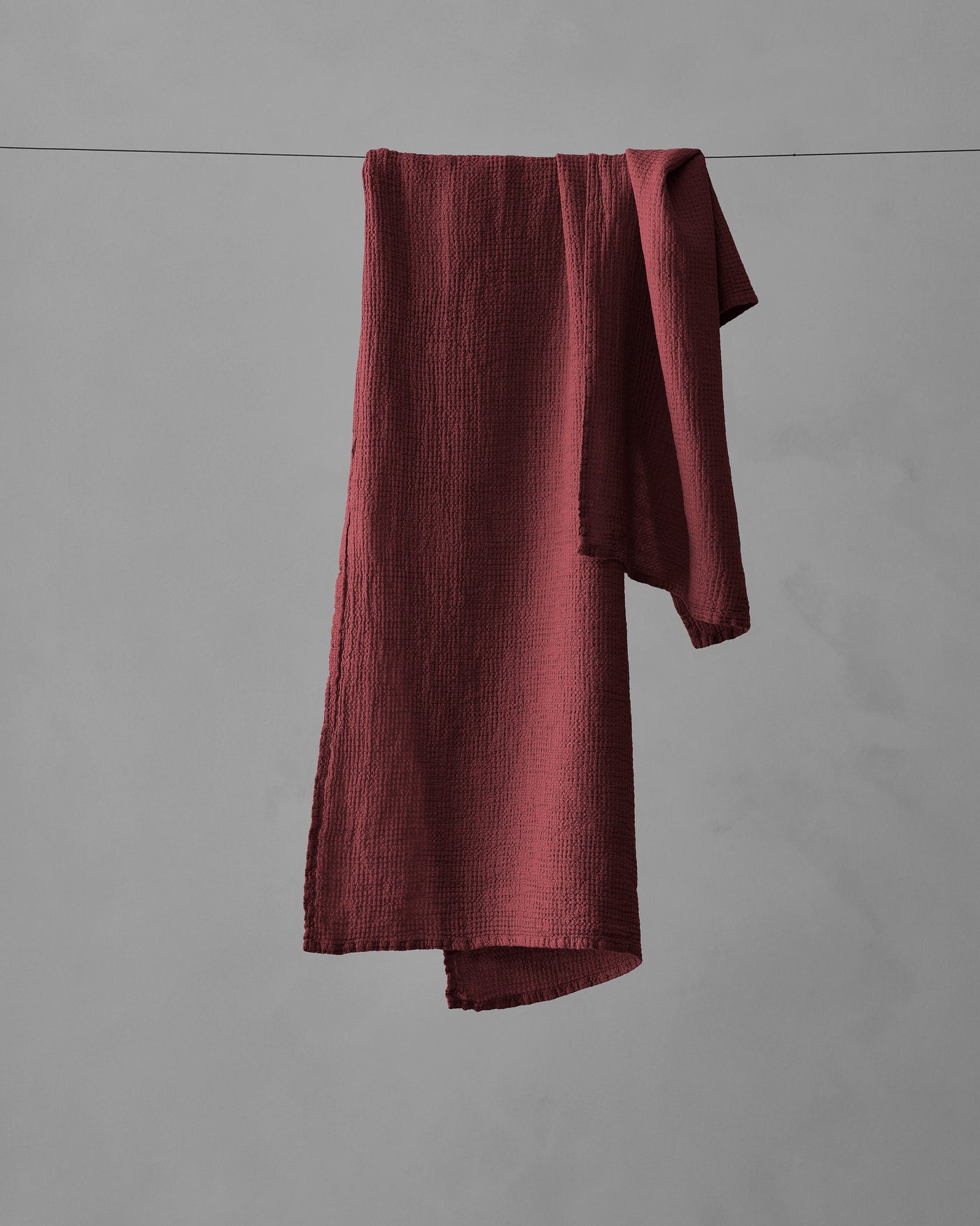 Crimson crinkle-textured cotton hand towel draped over a clothesline against grey background.