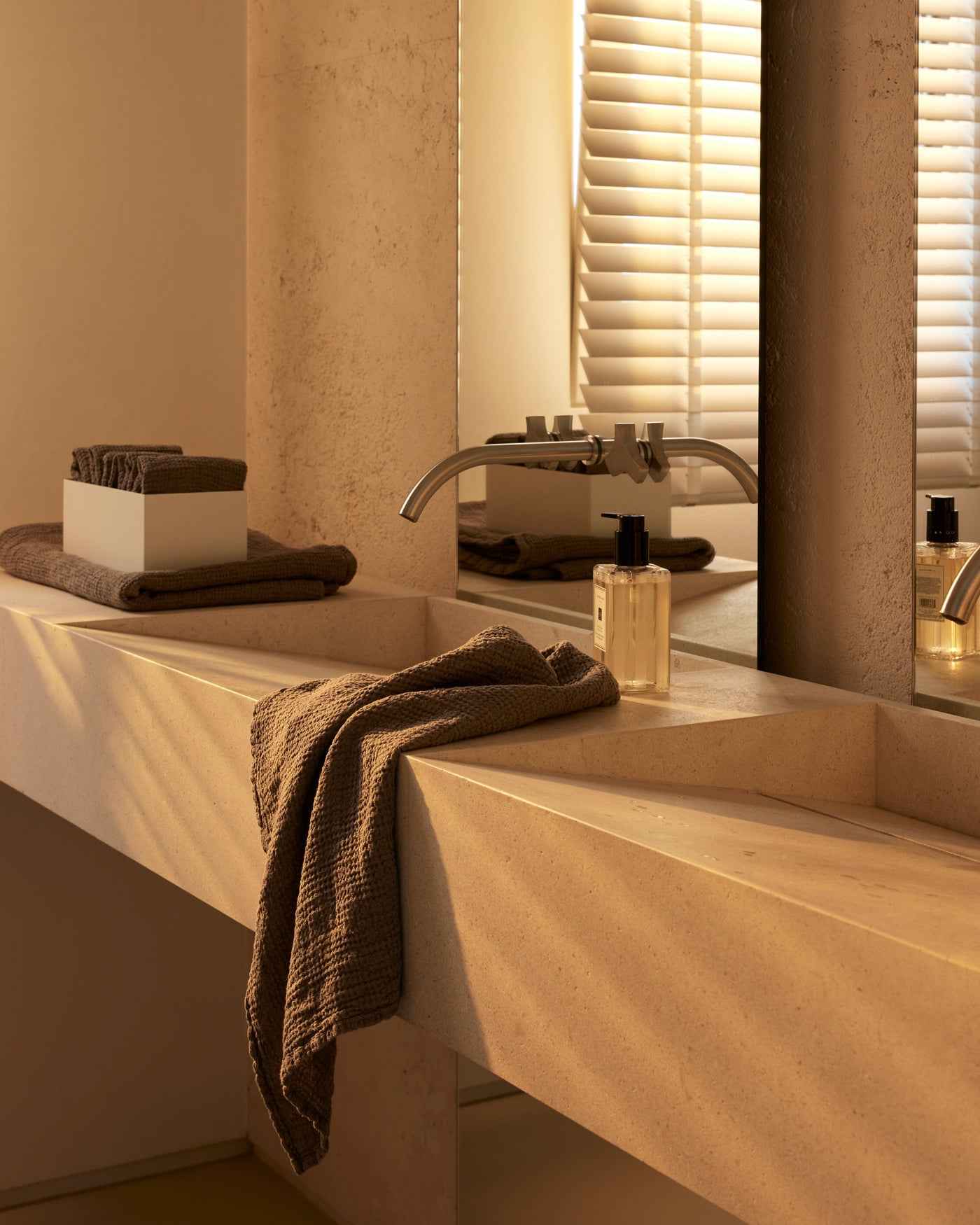 Mocha waffle-textured hand towel draped over a travertine sink edge in warm ambient light.