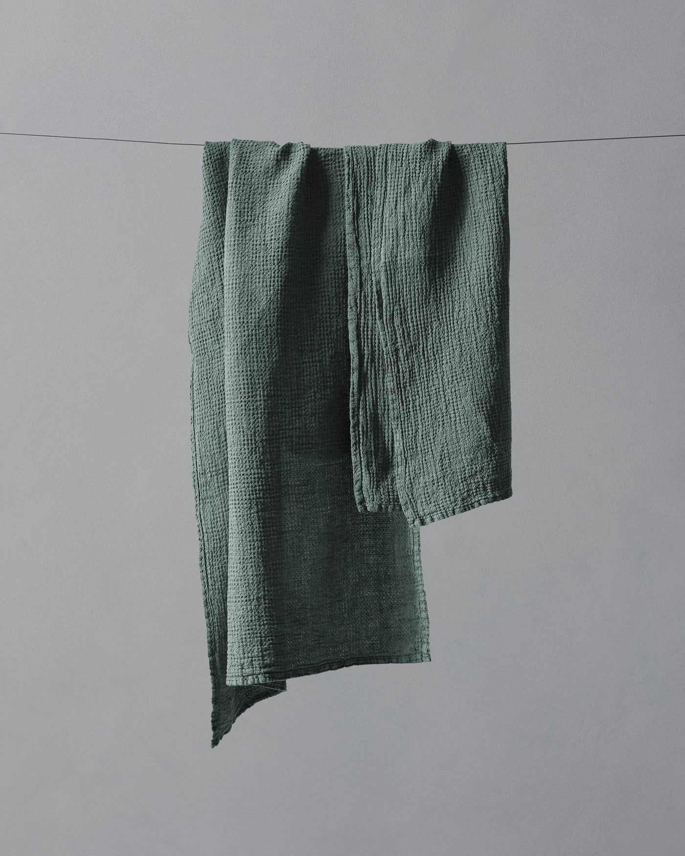 Sage green crinkled cotton gauze hand towel draped over a line against a grey background.