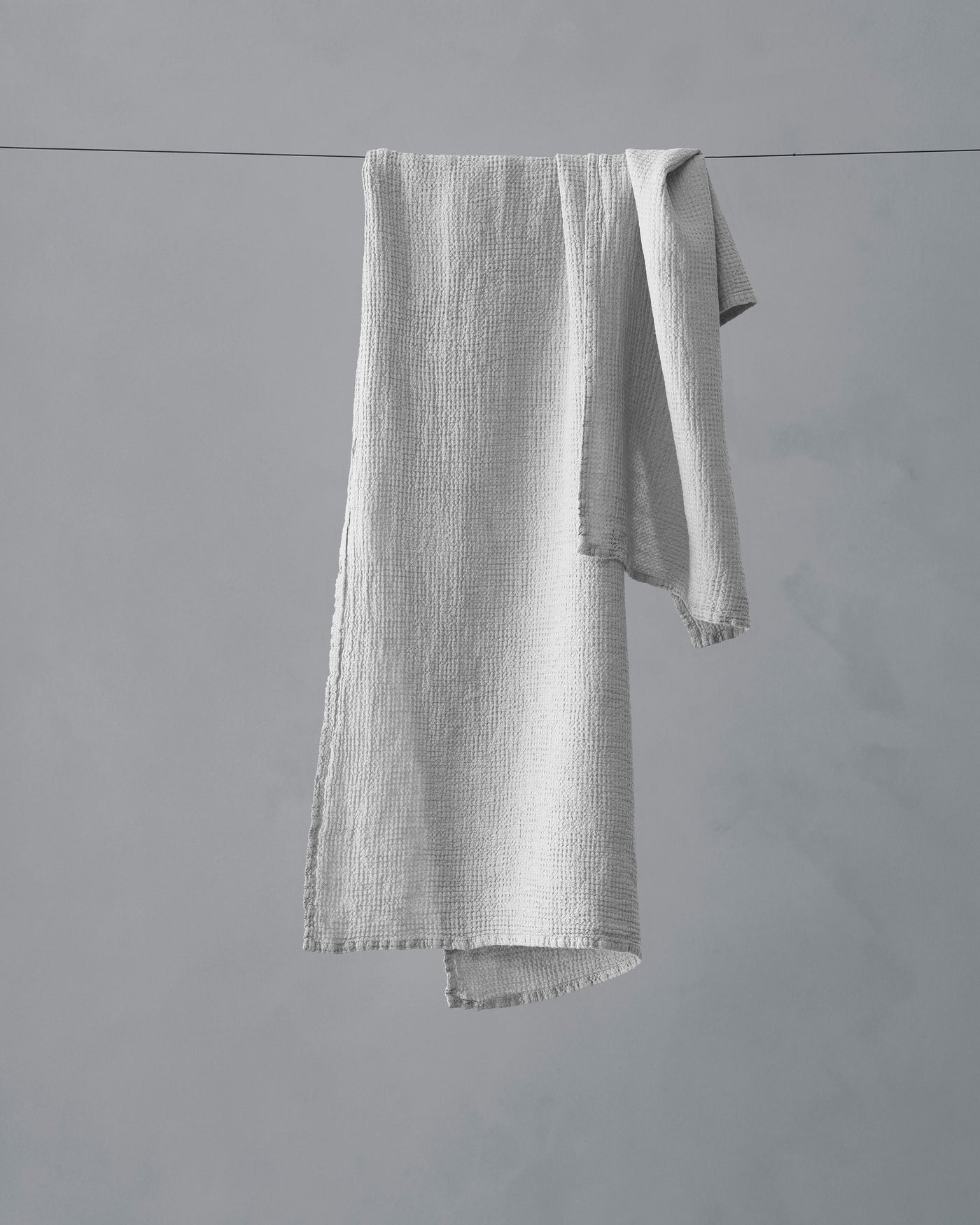 Society Limonta Lipe New hand towel in white draped over a clothesline, showing textured muslin weave and frayed edges.