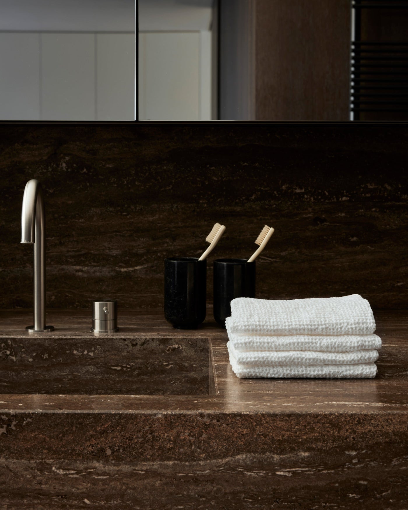 Society Limonta Lipe New ivory waffle-weave hand towels stacked on dark marble bathroom counter.