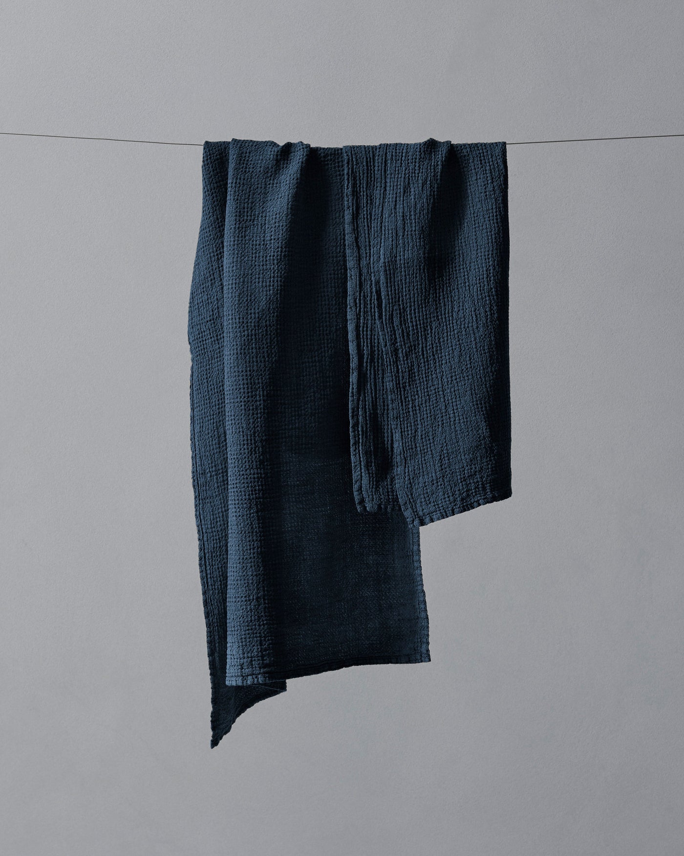 Midnight blue crinkled cotton muslin hand towel draped over a wire against grey background.