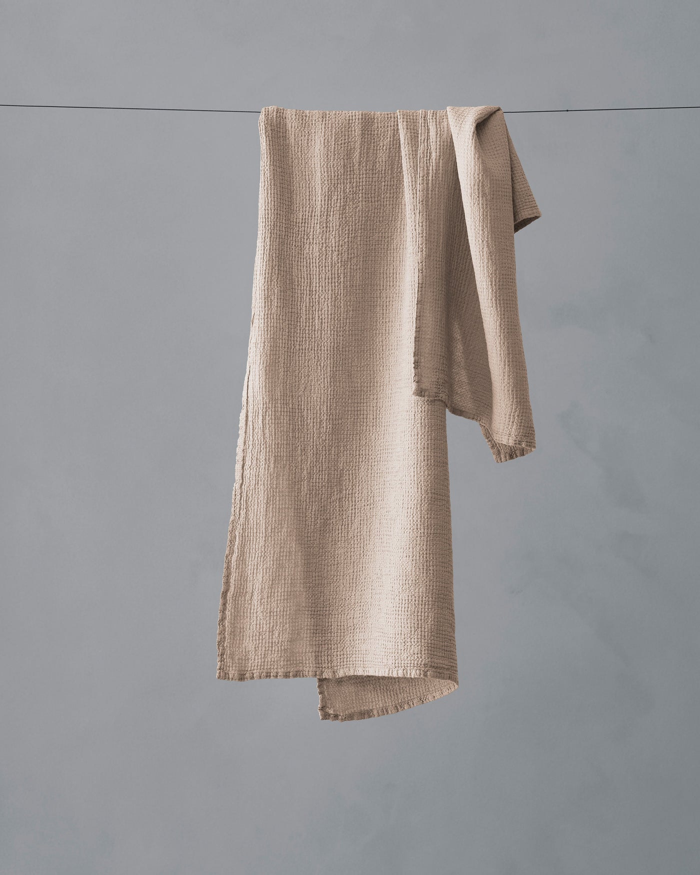 Society Limonta Lipe New hand towel in dune, draped over a clothesline showing frayed linen edge detail.