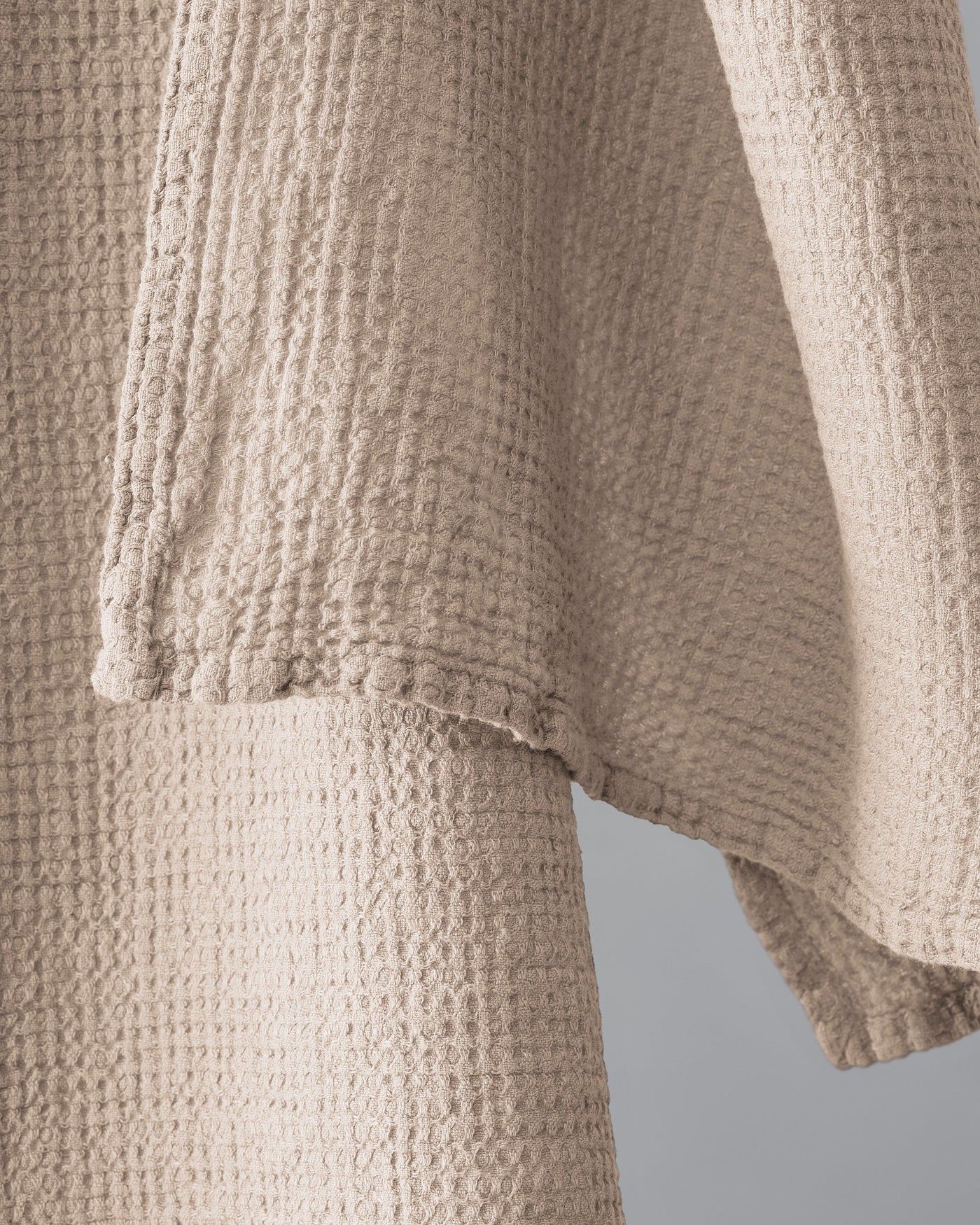 Close-up of waffle-weave texture and hemstitched edge detail in sand.