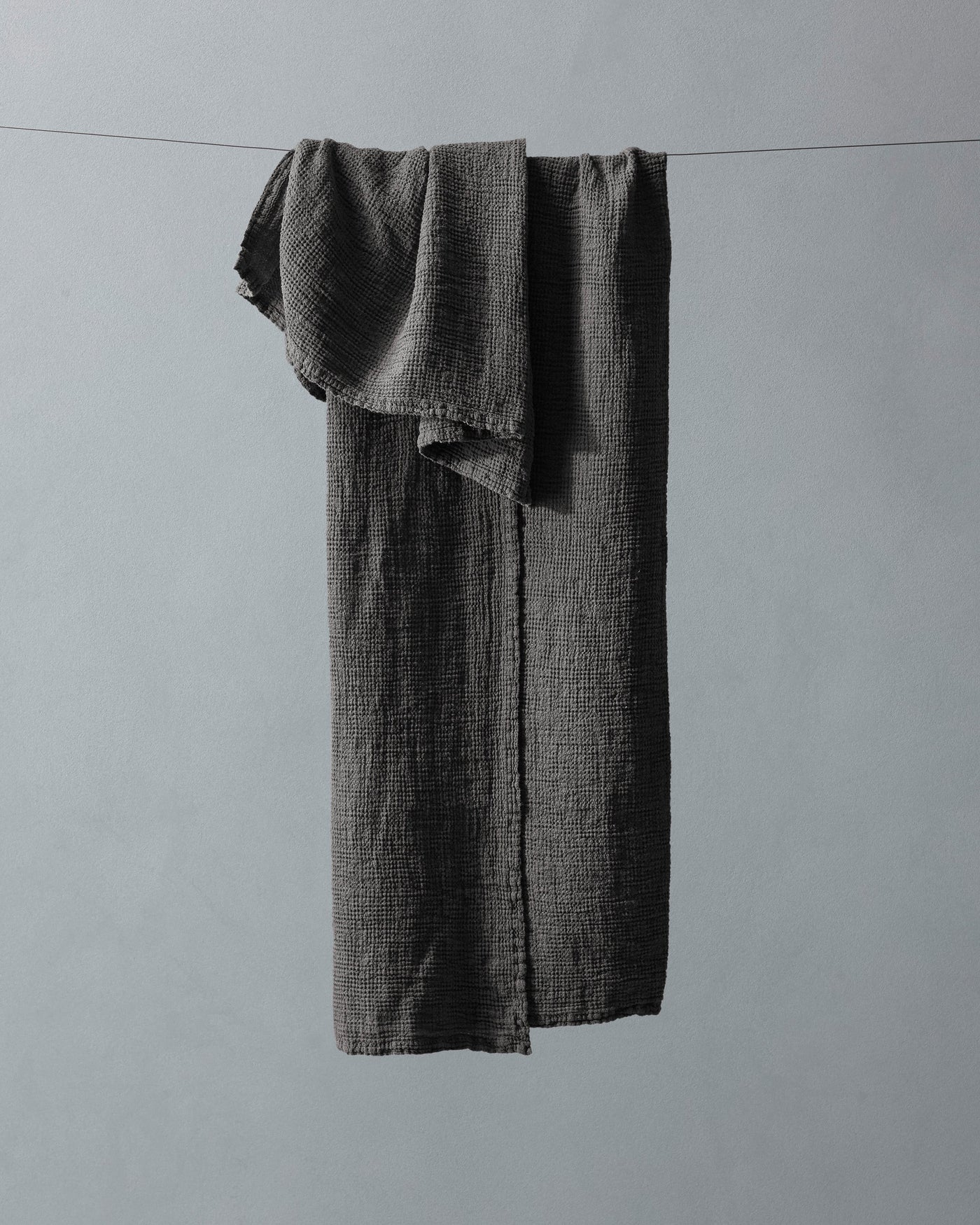 Charcoal textured cotton gauze bath towel draped over a thin wire, showing full length and frayed edges.