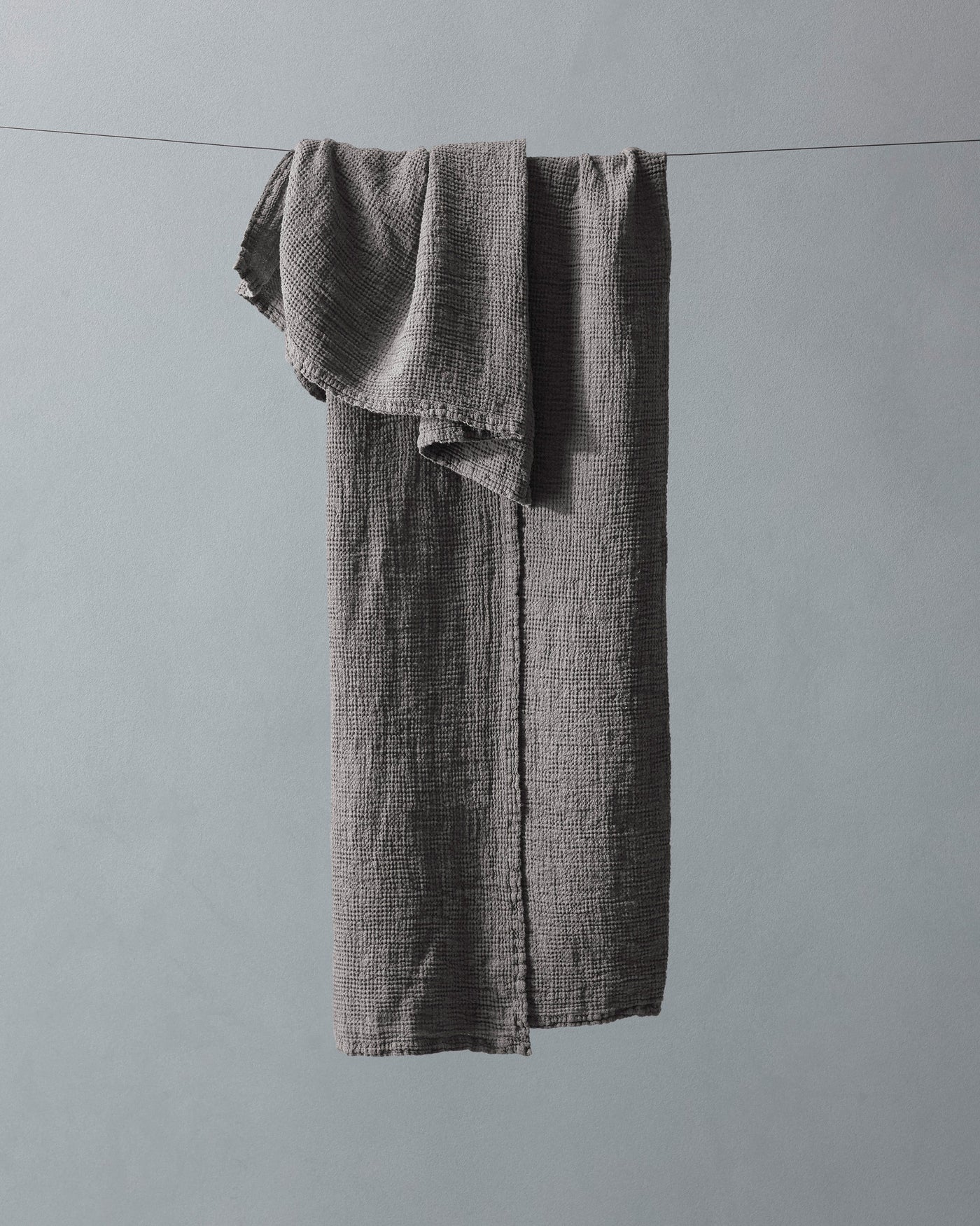 Charcoal textured linen bath towel draped over a clothesline, showing natural frayed edges.