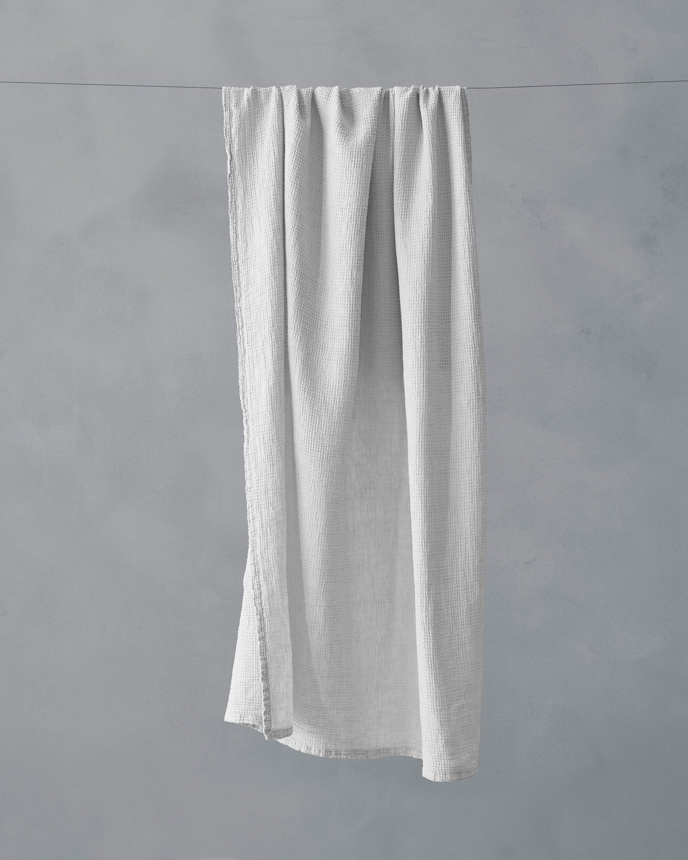 Society Limonta Lipe New bath towel in white linen hanging on a line against grey background.