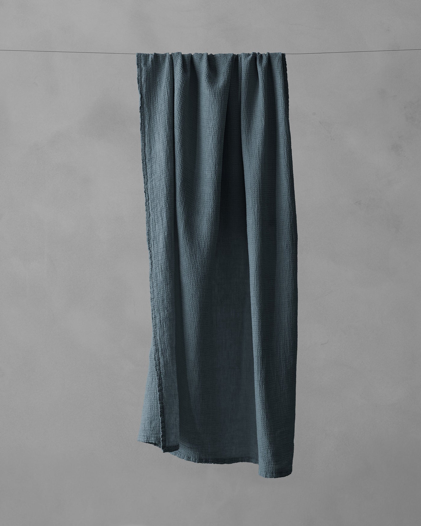 Society Limonta Lipe New bath towel in slate blue linen, draped over a clothesline.
