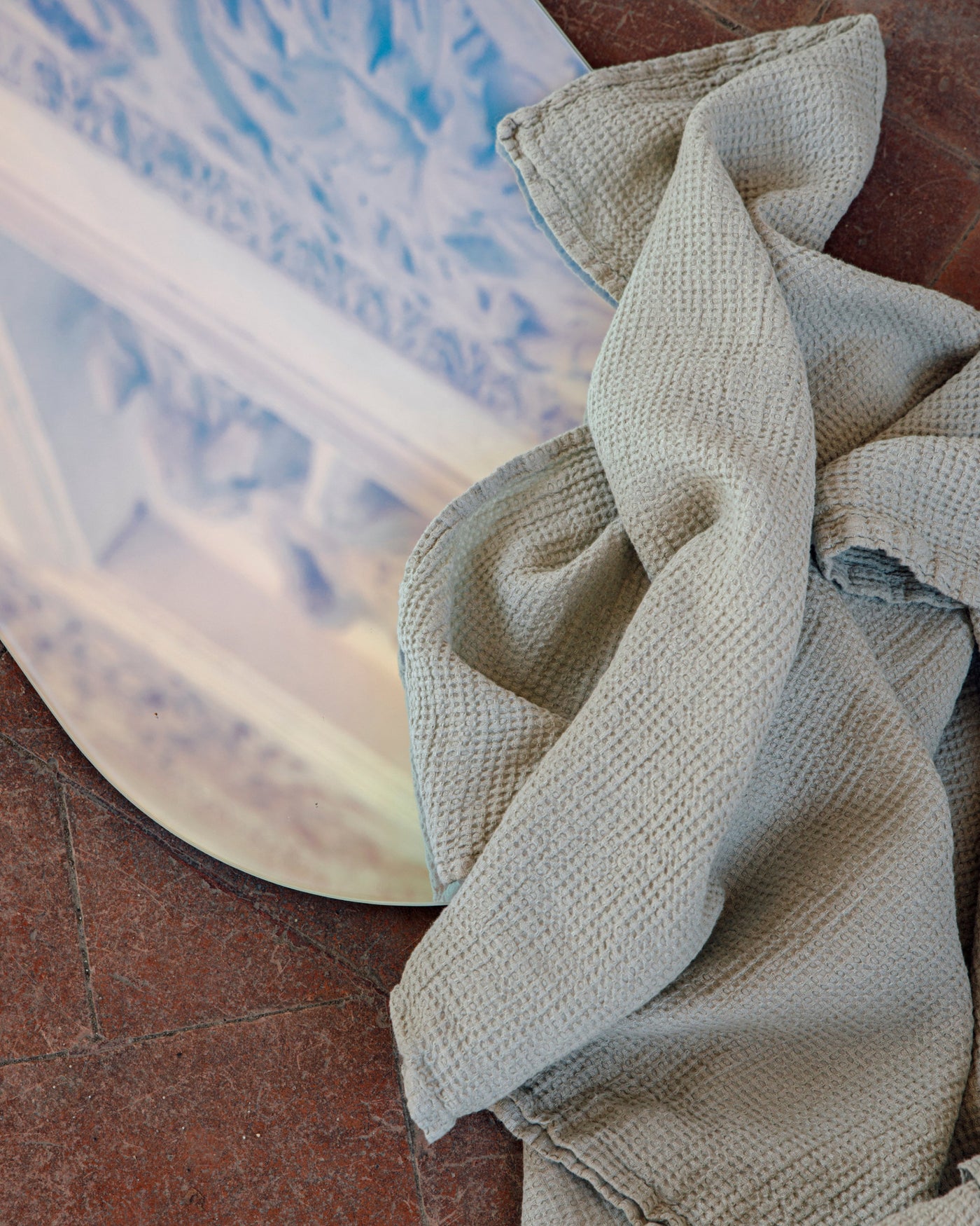 Close-up of Society Limonta Lipe New bath towel in sage, waffle texture draped loosely on terracotta floor.