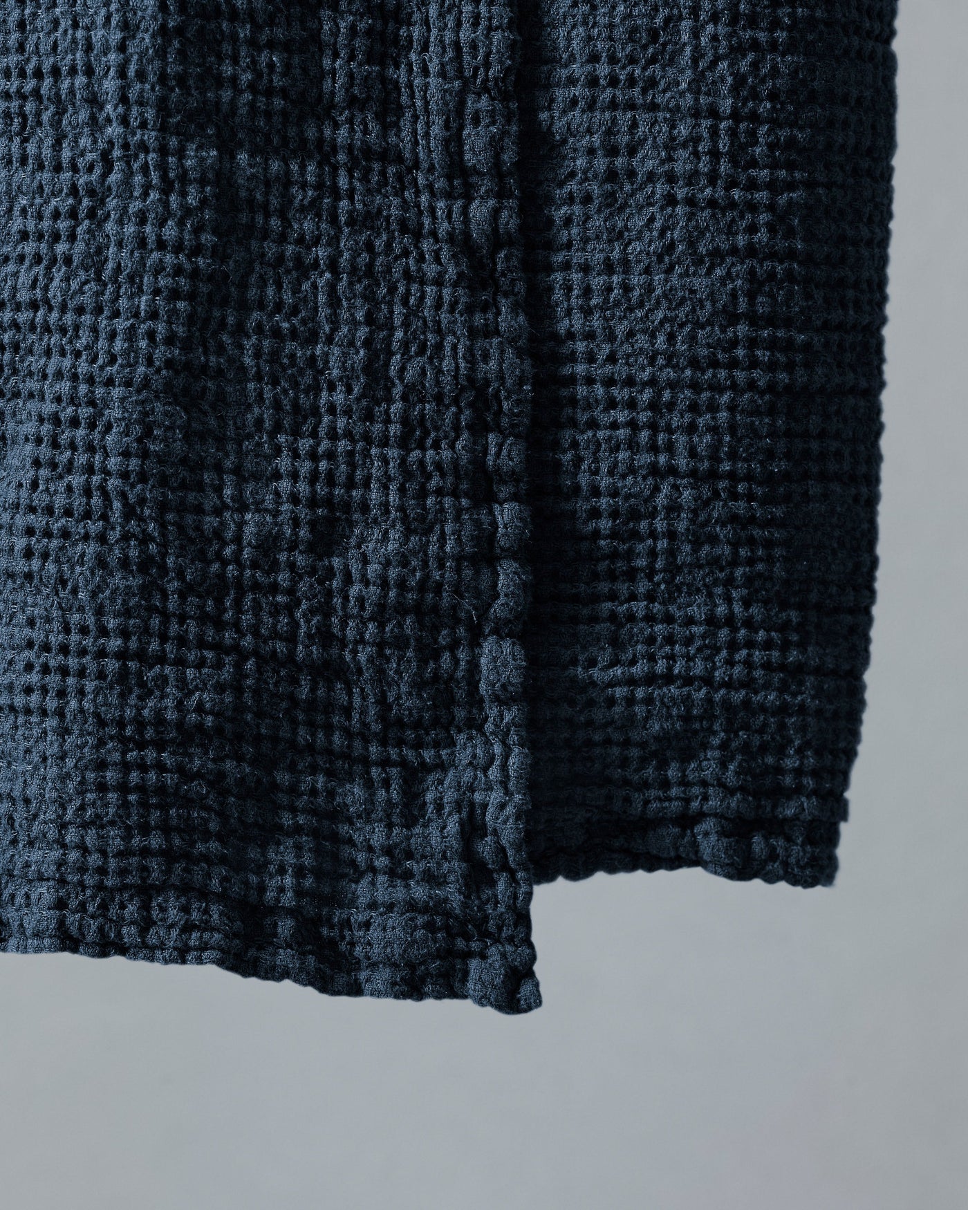 Close-up of midnight blue waffle-weave texture and hemmed corner of a bath towel.