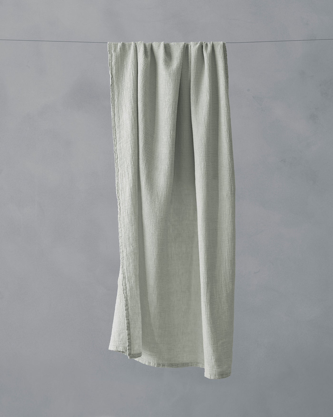 Close-up of Society Limonta Lipe New bath towel in sage, draped on a line showing frayed linen edges.