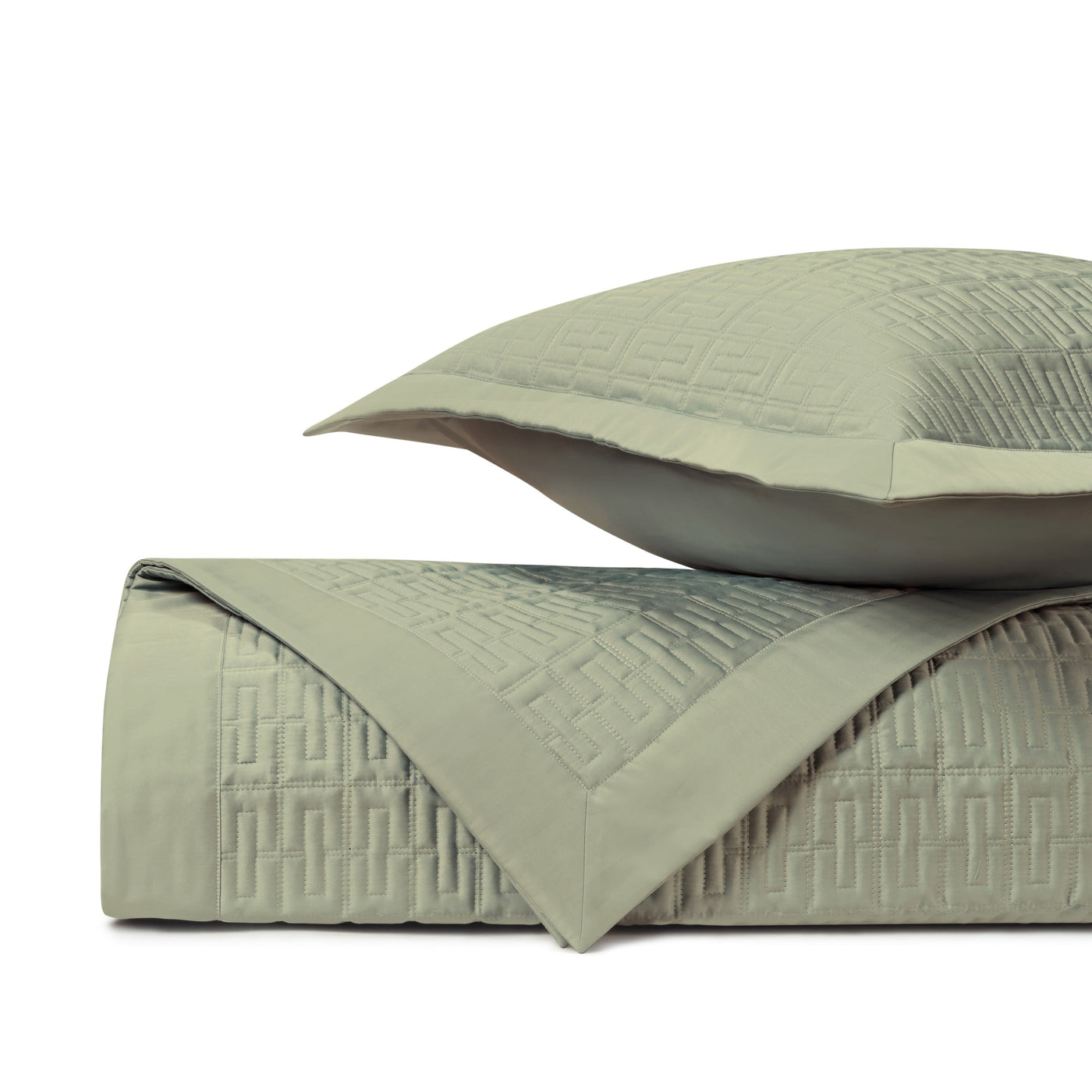 Close-up of sage green quilted coverlet with geometric maze pattern, folded with matching sham.