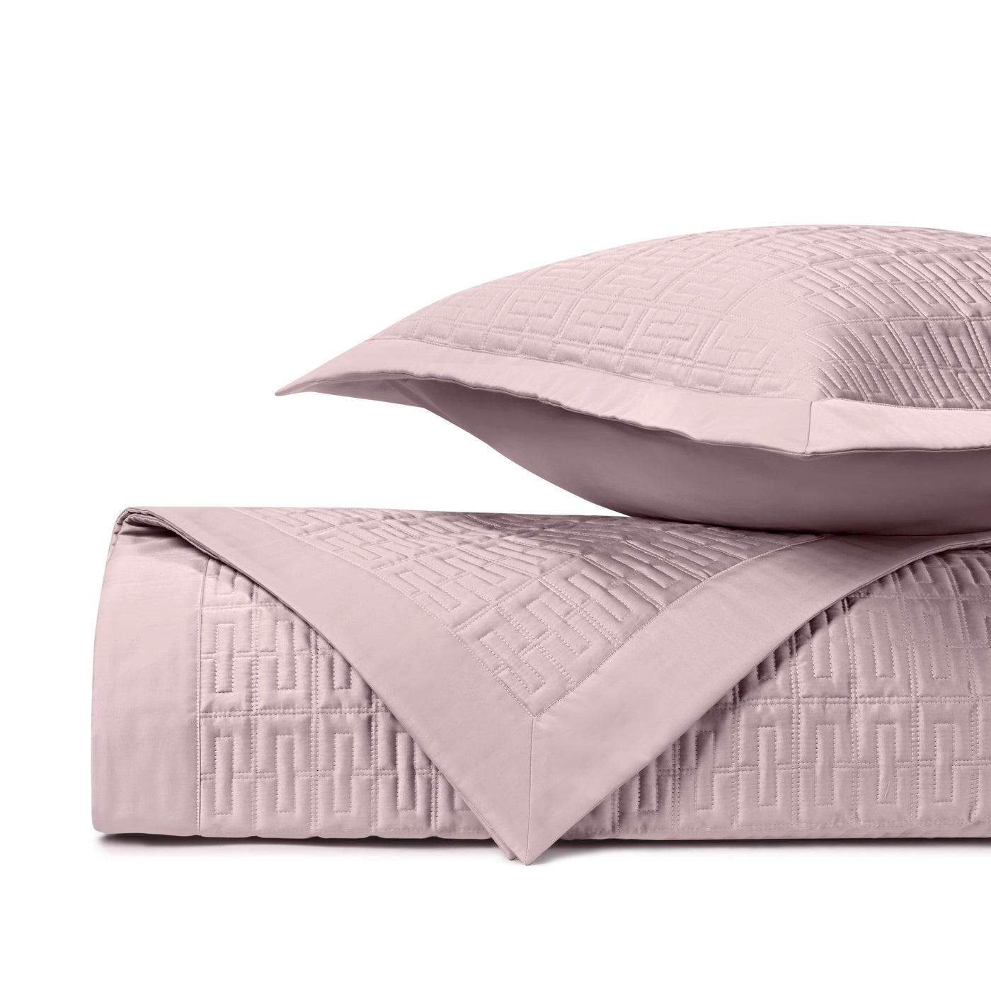 Blush quilted coverlet and sham with geometric Greek key stitching pattern, folded and stacked.
