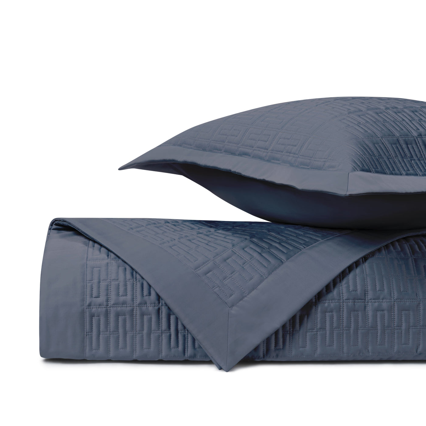 Close-up of navy quilted coverlet corner with geometric basket-weave stitching and matching sham.