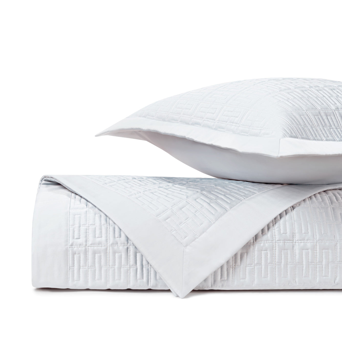 Close-up of white quilted cotton with a geometric fretwork pattern and border detail.