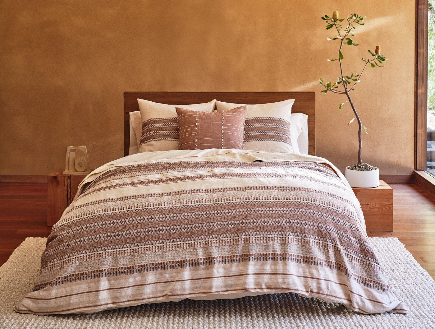 Coyuchi Precita duvet and terracotta throw pillows styled on bed in warm-toned room.