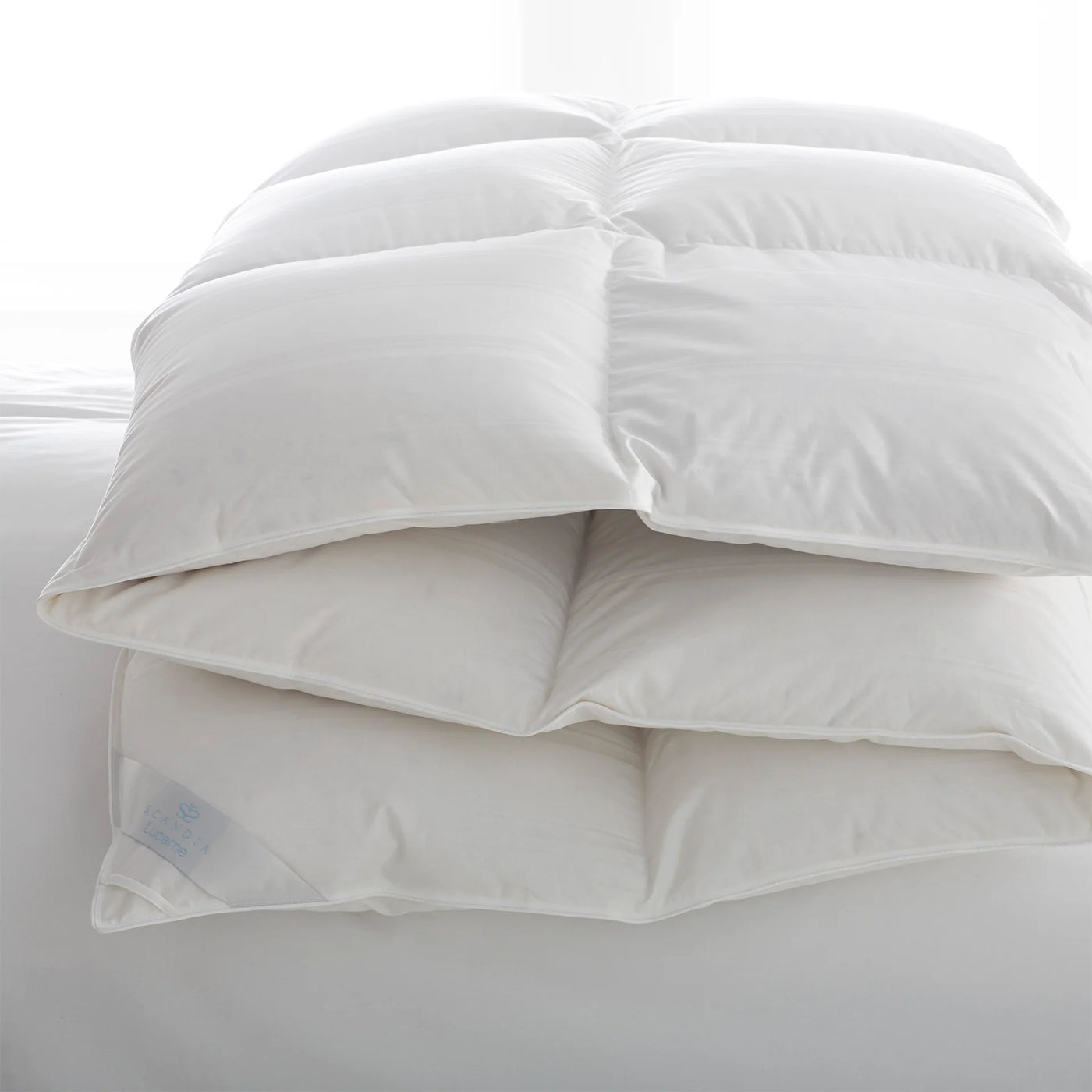 Scandia Home Lucerne white down duvet folded and stacked on a bed.