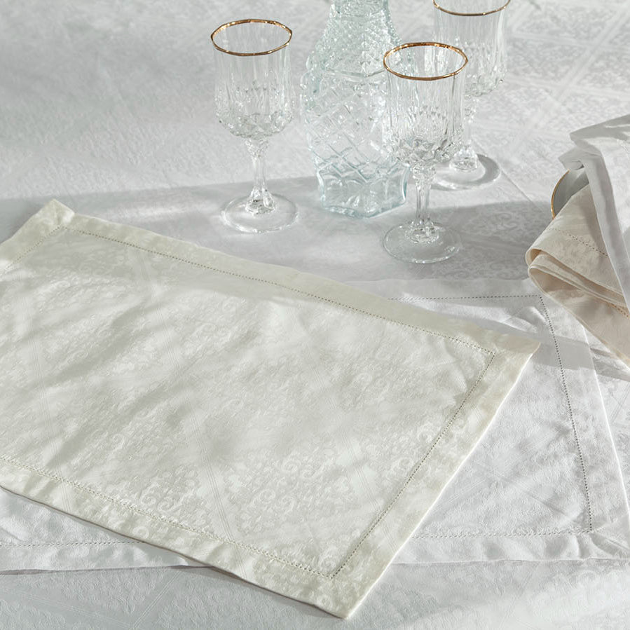 Ivory jacquard dinner napkin with bordered hem, styled on a white tablecloth setting.