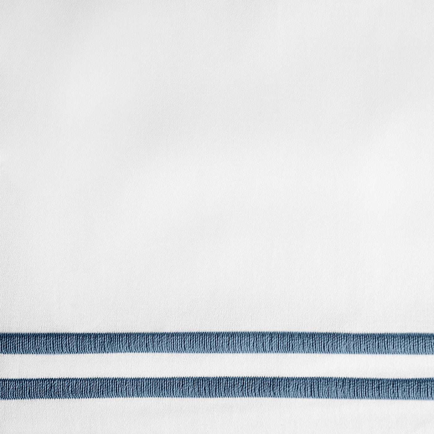 Close-up of twin navy embroidered border stripes on white linen fabric.